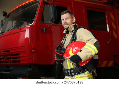 Firefighter in uniform with helmet near red fire truck at station - Powered by Shutterstock