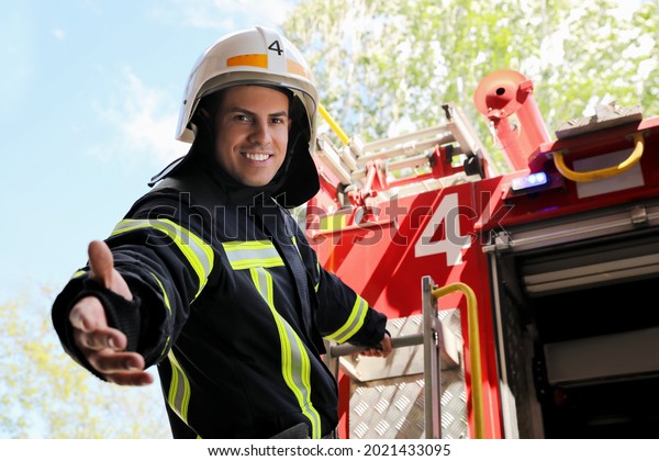 Firefighter in uniform and helmet offering hand\
near fire truck\
outdoors