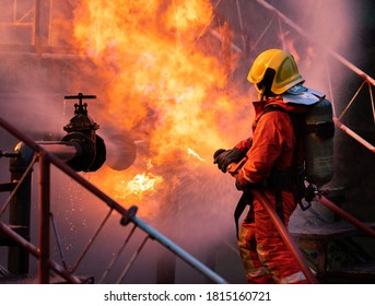 Feuerwehrleute, die einen Feuerlöscher mit Wassernebel verwenden, um mit der Flamme aus dem Leck der Ölpipeline und der Explosion auf der Ölplattform und in der Erdgasstation zu kämpfen. Konzept der Feuerwehr und der industriellen Sicherheit.