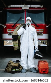 Firefighter in white protective, tyvek style suit, mask, and eye protection holding turnouts and medical gear during the Covid-19 pandemic.