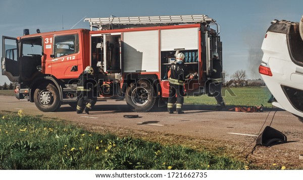 Firefighters\
Arrive on the Car Crash Traffic Accident Scene on their Fire\
Engine. Firemen Grab their Tools, Equipment and Gear from Fire\
Truck, Rush to Help Injured, Trapped\
People.