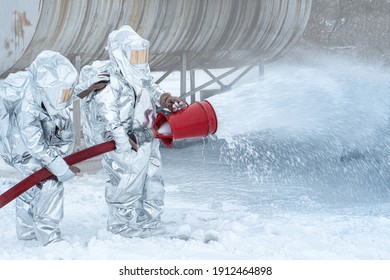 Firefighters In Fire Fighting Operation. Airport Firefighters. Training The Firefighters. In The Foreground Is A Drop Of Foam Springer, A Fireman Protects Fire Safety.