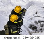 Firefighters in protective gear using a fire hose to spray foam during emergency response. Firefighting teamwork, safety, and rescue operation on a wet asphalt surface.