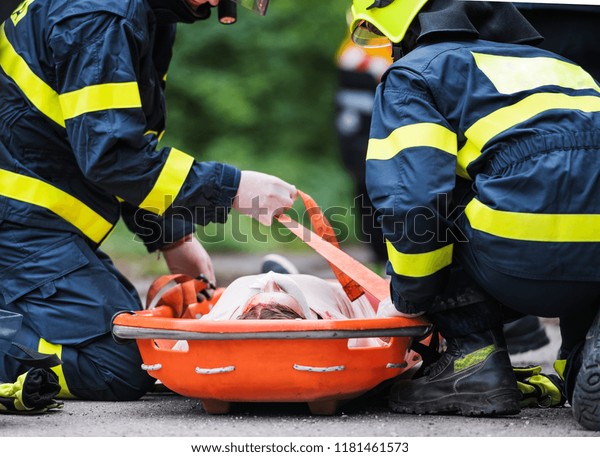 Firefighters putting an injured woman into a\
plastic stretcher after a car\
accident.