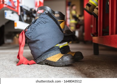 Firefighter's shoes and pants and a wardrobe cabinet, fire truck and fireman in the background