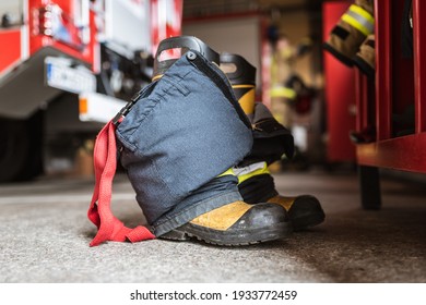Firefighter's shoes and pants and a wardrobe cabinet, fire truck and fireman in the background.