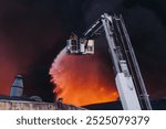 Firefighters use telescopic tower during massive large blaze fire, firetruck with a crane, firemen team putting out the fire with extendable fire ladder, blazing warehouse factory, burning building