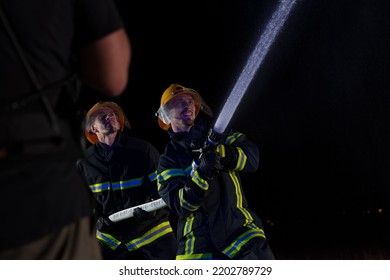 Firefighters Use A Water Hose To Eliminate A Fire Hazard. Team Of Firemen In The Dangerous Rescue Mission.