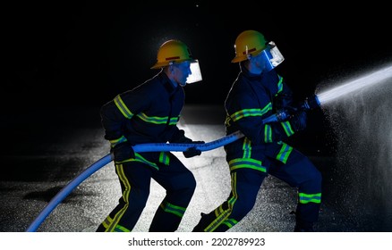 Firefighters Use A Water Hose To Eliminate A Fire Hazard. Team Of Firemen In The Dangerous Rescue Mission.