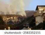 Firefighters work tirelessly as smoke billows from the Franklin Fire near a house in Malibu, California, battling the wildfire