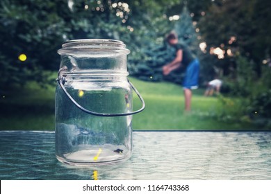 Fireflies In A Jar On A Table With Kids Catching More In The Background