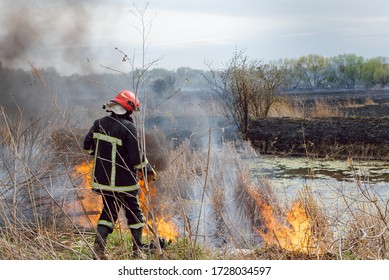 Fireman Or Firefighter Backburning And Extinguishing A Wildfire Grass And Bushfire. Closeup Of Voluteer Battling An Out Of Control Grass Fire.