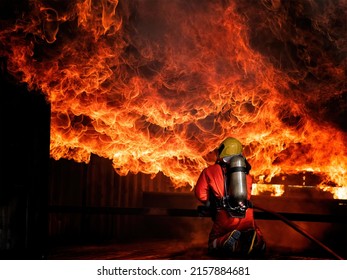 Fireman or firefighter from fire wearing fire protection suit and helmet and breathing with oxygen tank hold the water hoses spraying water to extinguish the heavy fire burn and smoke overhead