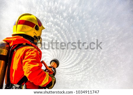 Fireman or Firemen in fire fighting equipment, Firefighter using extinguisher and spray water from hose for fire fighting, Firefighter spraying high pressure water to fire with copy space.