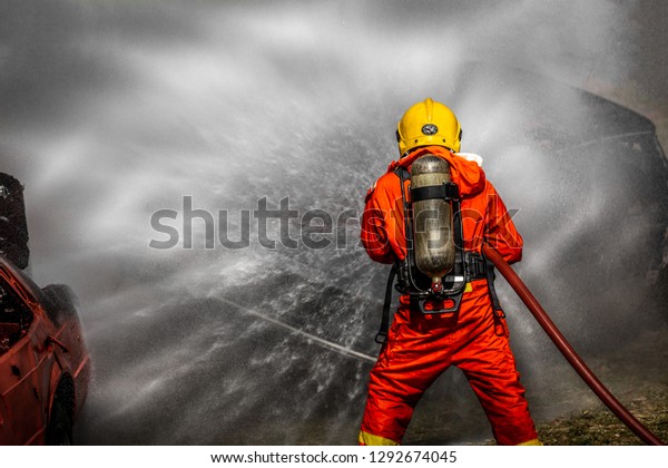 Fireman or Firemen in fire fighting equipment,\
Firefighter using extinguisher and spray water from hose for fire\
fighting, Firefighter spraying high pressure water to fire with\
copy space.
