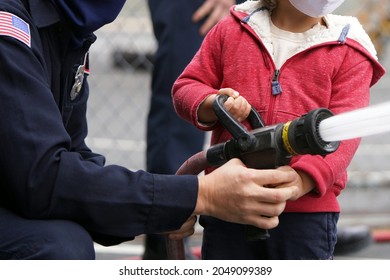 Fireman in uniform shows a child how to use the fire hose from his firetruck outside squirting water in a parking lot                                - Powered by Shutterstock