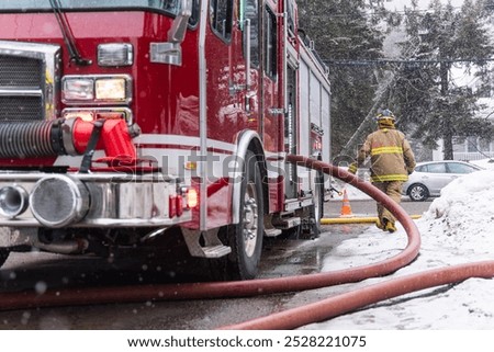Fireman is walking through the snow pulling a large fire hose away from the firetruck during a snowstorm. Selective focus