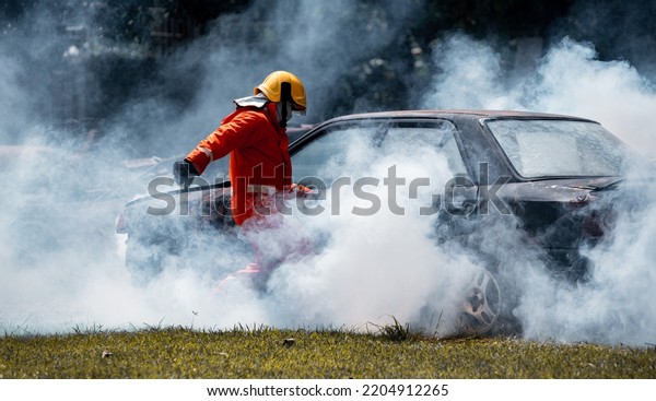 Fireman wearing safety\
uniform help car crash accident for rescue victim life on fire and\
thick smoke area fire safety accident protection is industry safety\
concept.