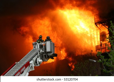 Firemen on a crane against wall of fire