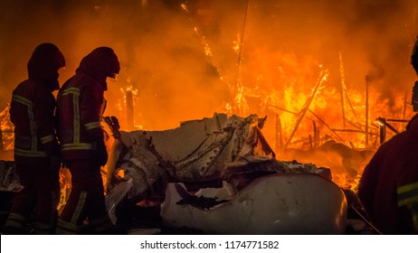 Firemen In Professional Uniform In Front Of The Burning Structure, Fire Of A Falla Sculpture Made Of Paper At Las Fallas Festival In Cullera, Valencia, Spain.