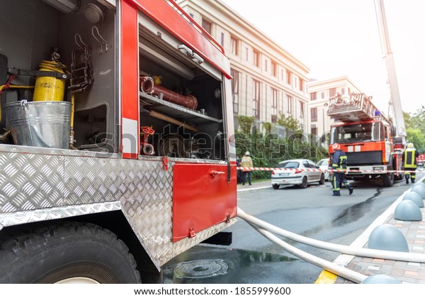Firemen wearing uniform standing behind fire\
tape and many fire engine trucks with ladder at accident in\
highrise tower residential or office building in city center.\
Emergency rescue at\
disaster