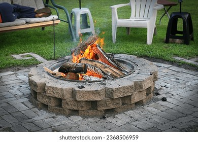 Firepit. Bonfire. Flames. Outdoor living. Leisure. Backyard. Trailer. Lawn chairs. Logs. Wood. Summer. Summertime. Get together. Friends. Bricks. Campfire. Green grass. 
