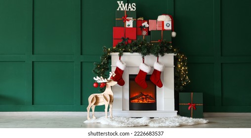 Fireplace with Christmas gifts, socks and wooden deer near green wall in room - Powered by Shutterstock