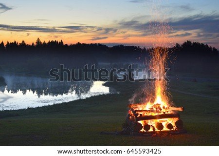 Fireplace hipe and stack and midsummer festival fire flames on the hill near the lake at sunny summer evening