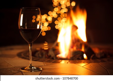 Fireside With A Glass Of Wine - A Relaxing Environment Near The Fire, Enjoying A Glass Of Red Wine With Some Bokeh Lights In The Background.