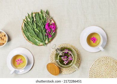 Fireweed tea in white cups and transparent glass teapot, herbal hot tea from green leaves of ivan chai on textile linen tablecloth. Top view healthy drink and wild flowering willow-herb, tea time
