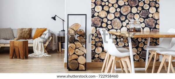 Firewood next to white chairs and dining table with liqueurs in room with sofa and wooden stool