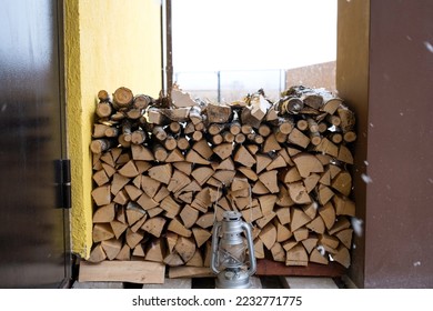 The firewood on the snowy porch of the house is harvested for the winter. Heating of housing with a stove fireplace, saving electricity and gas in a crisis, environmental friendliness. - Shutterstock ID 2232771775