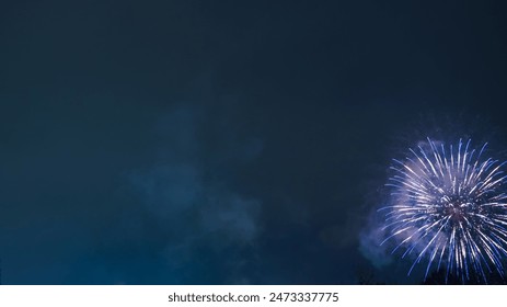 Fireworks exploding in the night sky. Blue and white fireworks create a stunning contrast against the dark sky. A symbol of festivity and celebration