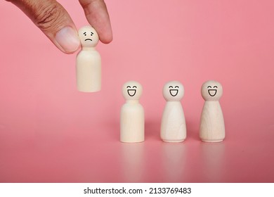 Firing, Bad Employee And Demotion Concept. Hand Pick Wooden Doll With Sad Face Icon. Pink Background