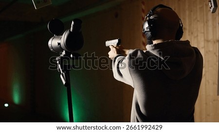 Firing range customer doing shooting activity with pistol, looking in zooming device to check if he shot bullseye. Person in shooting gallery analyzing targets shot using magnifying lens, camera A