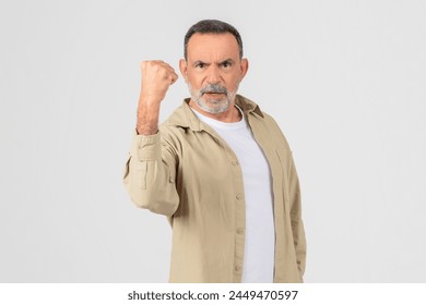 A firm and resolute elderly man clenches his fist, isolated on a white background, feeling angry, have fight