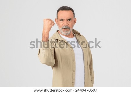 A firm and resolute elderly man clenches his fist, isolated on a white background, feeling angry, have fight