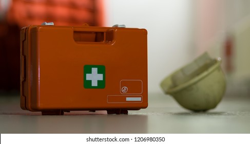 First Aid After An Accident At Work. First Aid Kit And Helmet Near Worker.