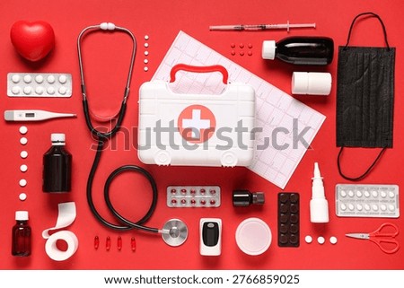 First aid kit with cardiogram, different medical supplies and pills on red background