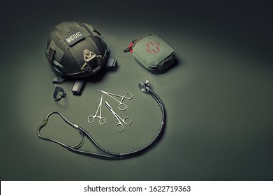 First Aid Kit, Phonendoscope, A Set Of Scissors With A Helmet Lie On A Green Background. View To The Top. Military Medicine Concept