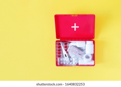 First aid kit red box with medical equipment and medications for emergency top view on pastel yellow background. Copy space.