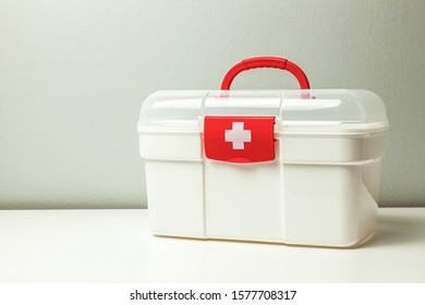 First Aid Kit. White Box With A Cross And A Red Clasp On A Gray Background.