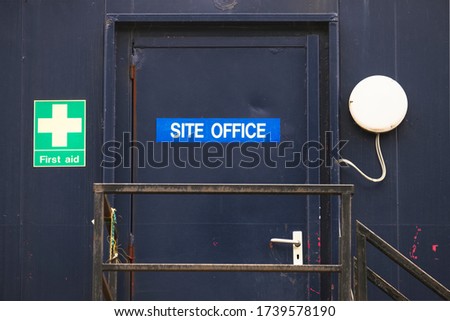 First aid site office sign on construction building door railing for workplace health and safety green cross