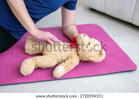 first aid training, CPR practice, cardiopulmonary resuscitation, emergency response, life saving technique, infant simulation, child safety education, teddy bear model, plush toy, soft fabric texture, beige fur surface, red bow accent, training substitute, learning scenario, kneeling posture, adult hands, arm support, torso pressure, chest compression position, instructional demonstration, home environment, indoor setting, carpeted floor, pink exercise mat, foam padding, safety practice space, caregiver role, parenting skills, childcare preparation, emergency preparedness, basic life support, nonverbal instruction, physical guidance, close-up framing, partial body view, cropped subject, casual clothing, blue shirt fabric, neutral lighting, realistic training moment, educational concept, safety awareness, family protection theme, domestic interior, calm atmosphere, controlled movement, instructional photography, health education imagery, prevention training, rescue technique simulation
parental care concept, emotional preparation, baby expectation theme, future parent mindset, nurturing behavior, gentle touch, protective gesture, caregiving instinct, maternal readiness, paternal readiness, family planning idea, newborn anticipation, infant well-being focus, responsibility awareness, early bonding symbolism, tenderness expression, calm reassurance, emotional connection, caregiving practice, learning confidence, preparedness feeling, soft interaction, supportive posture, safety concern, health protection mindset, preventive education, responsible parenting values, home comfort, domestic calm, warmth atmosphere, trust building, caregiving routine concept, baby arrival preparation, child-focused thinking, nurturing environment, emotional security theme, compassion display, loving attention, early parenthood vision, care-oriented lifestyle, family growth symbolism