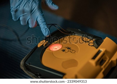 First aid training – The instructor is showing the Shock-button to press. the background is blurred. The focus is on the AED and the shock button. the picture is very detailed.