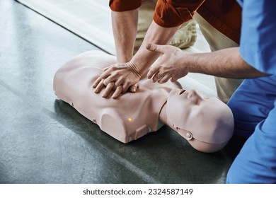 first aid training seminar, partial view of medical instructor pointing with hand and assisting man doing chest compressions on CPR manikin, life-saving skills and techniques concept - Powered by Shutterstock