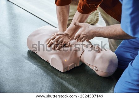 first aid training seminar, partial view of medical instructor pointing with hand and assisting man doing chest compressions on CPR manikin, life-saving skills and techniques concept