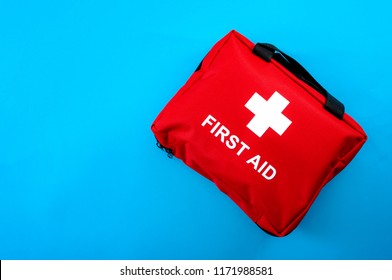 First aid treatment and medical emergency response concept with flat lay view of a red with a white cross first aid kit isolated on blue background with copy space for text