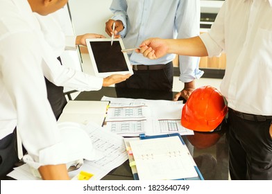 The First Asian Engineering Team Working On Construction Plans They Stand At The Table Near The Blueprint. The Two Men Pointed To The IPad.