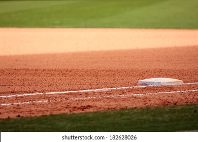 First Base Is Featured In Empty Baseball Field, Showing Infield Dirt And Outfield Grass.